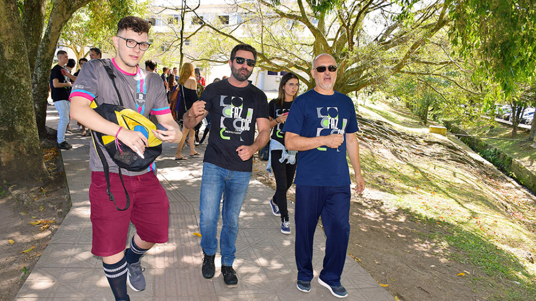 Uma foto de corpo inteiro mostrando três homens em evidência e mais pessoas no fundo.